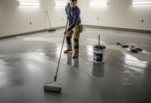 Person applying epoxy coating to concrete garage floor using paint roller with anti slip additives mixed in