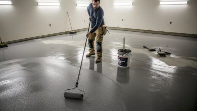 Person applying epoxy coating to concrete garage floor using paint roller with anti slip additives mixed in