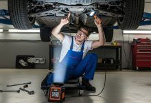 Mechanic inspecting vehicle undercarriage on hydraulic lift for impact damage and component wear