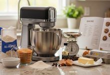 Modern stand mixer with stainless steel bowl on kitchen counter surrounded by baking ingredients