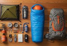 A hiker’s camping gear laid out on a wooden floor, including a tent, sleeping bag, backpack, and cooking tools organized by category