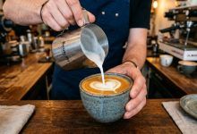 Barista pouring frothed oat milk into a ceramic coffee mug.