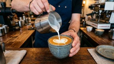 Barista pouring frothed oat milk into a ceramic coffee mug.