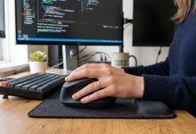 Ergonomic vertical mouse on a wooden office desk next to a laptop. (